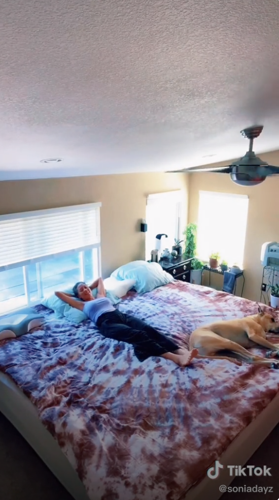 A woman lying on her Alaskan king bed with her dog, looking completely minuscule