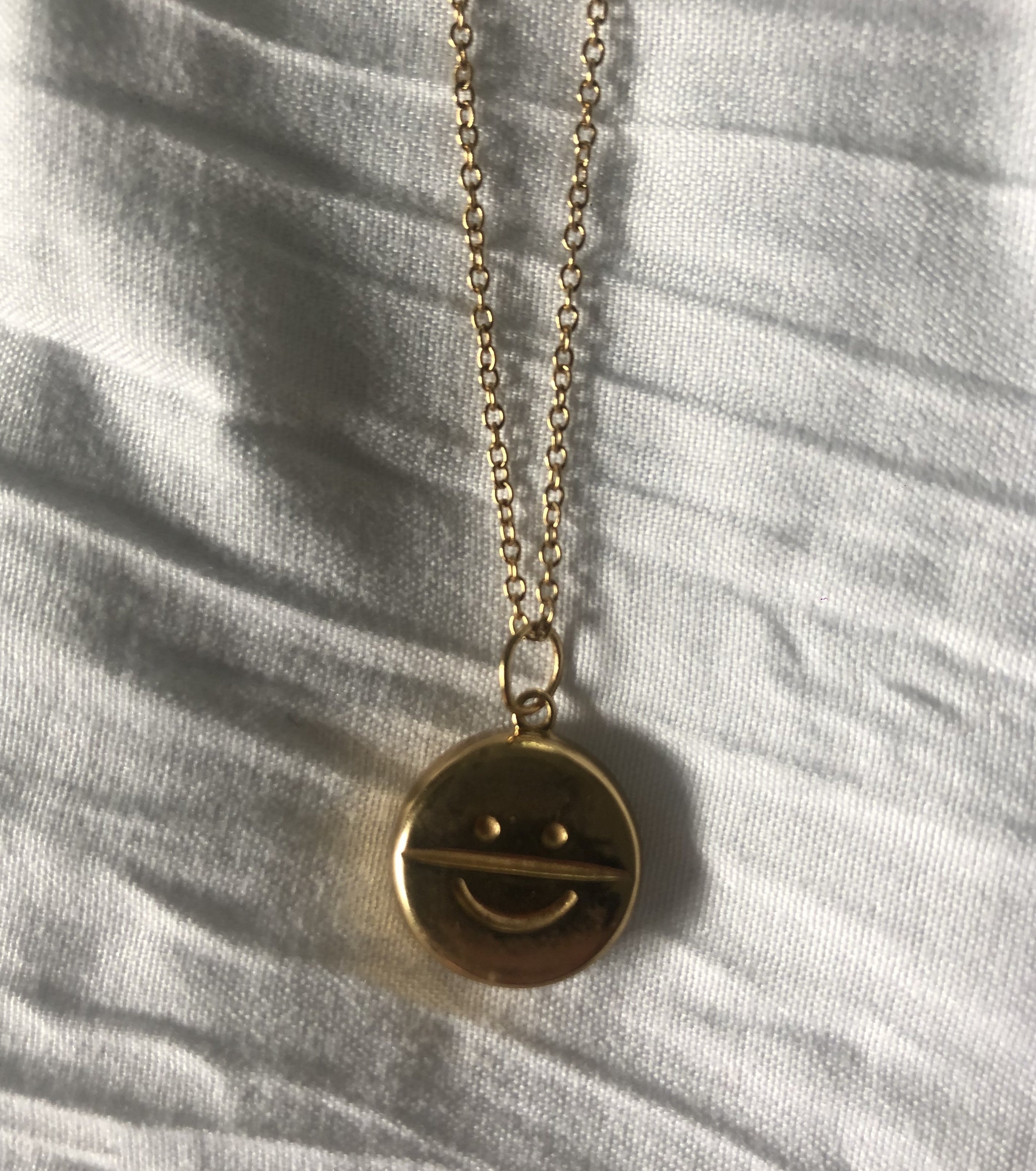 gold necklace with a gold charm of a smiley face on an antidepressant pill