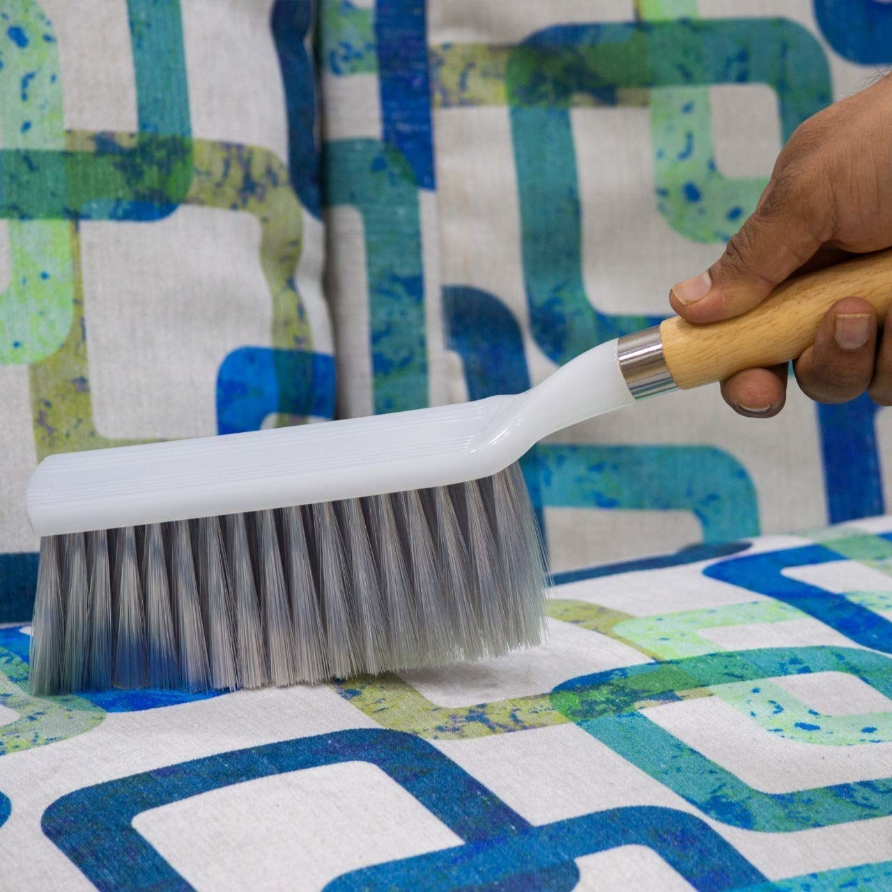 A person using a white-long bristled brush on a blue and white sofa 