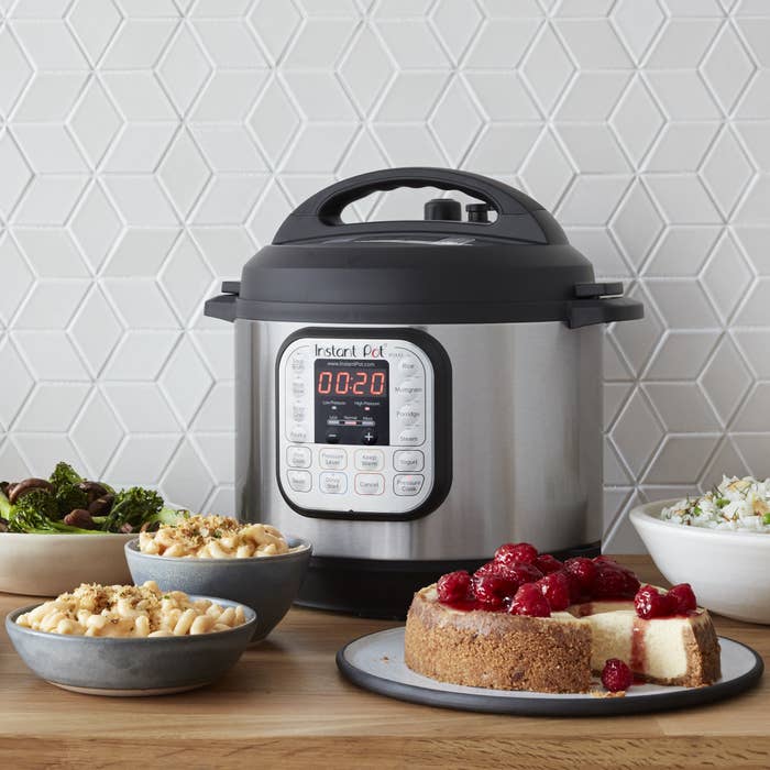 silver instant pot on a table next to pasta and cheesecake