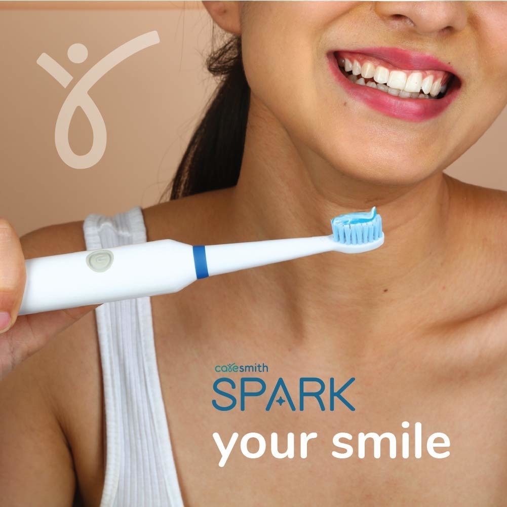 A woman smiling as she holds the electric toothbrush up 