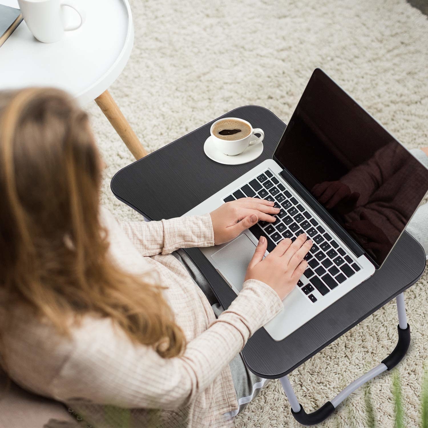 A woman typing on a laptop on a lap desk 