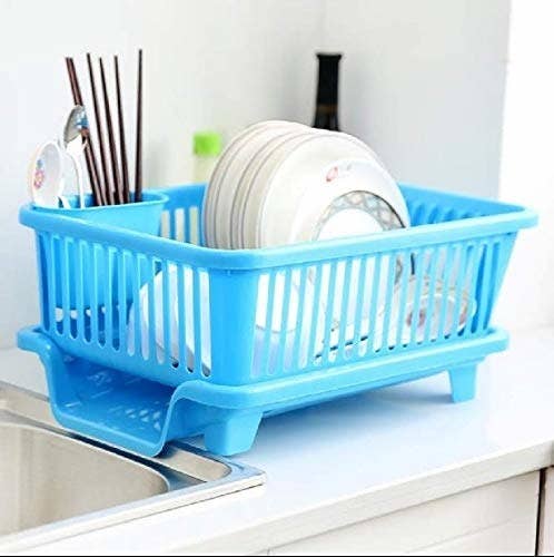 A blue dish drying rack by the kitchen sink with dishes in it