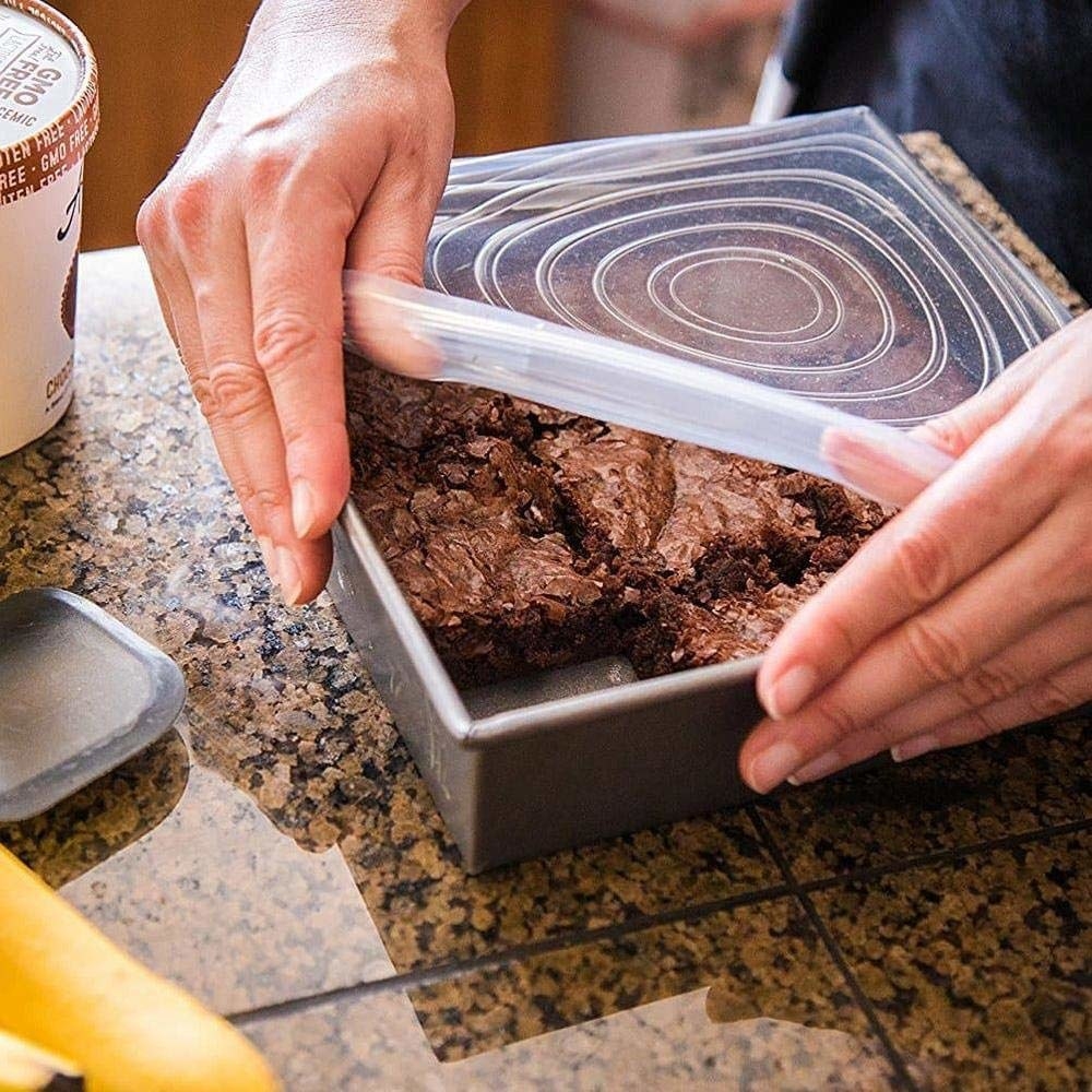 A hand covering a tray of brownies with the silicone lid 