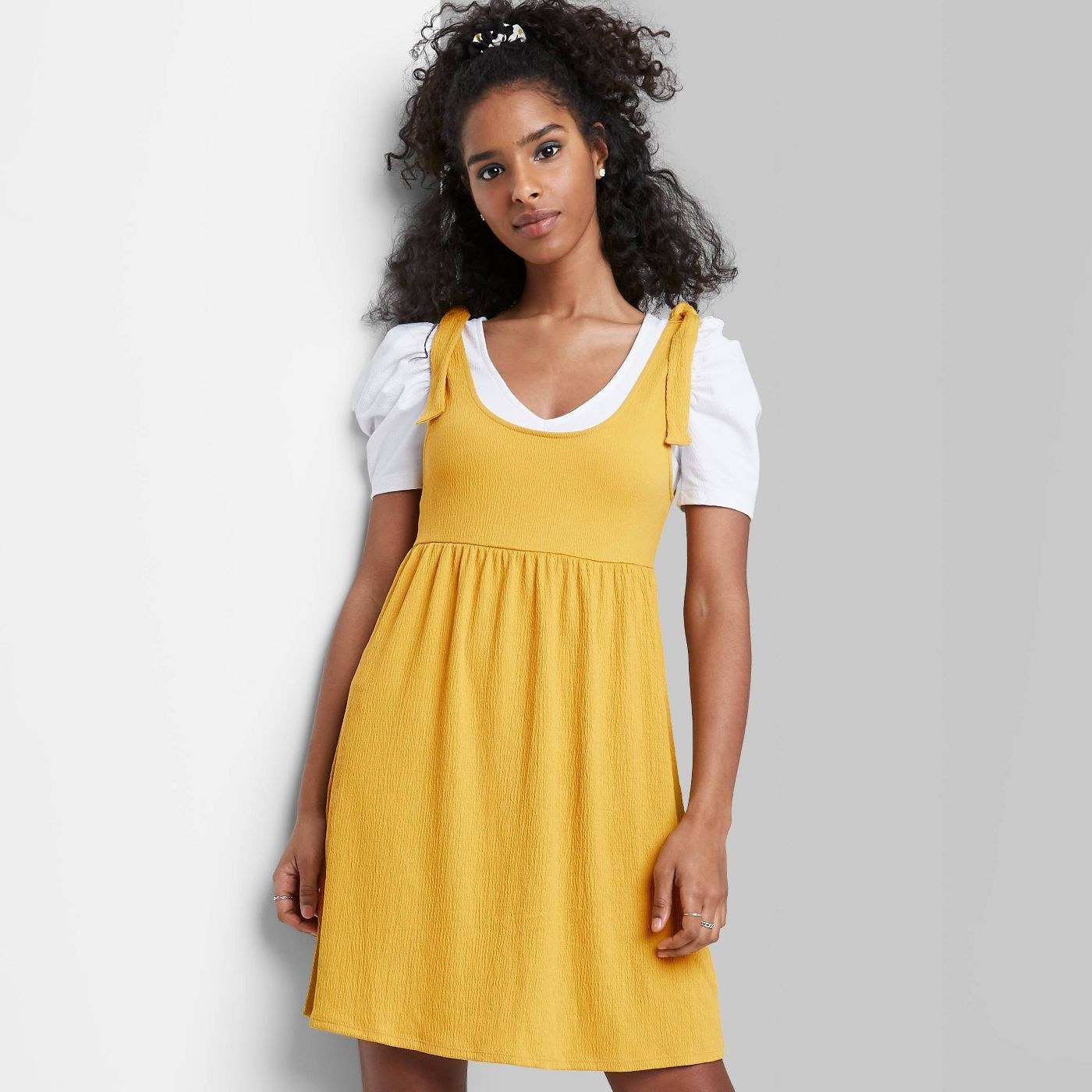 Model wearing yellow sleeveless dress, stops above the knee