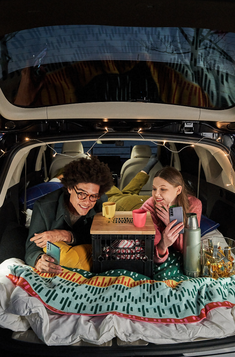 A man and a woman laying in the back of a car looking at a phone.