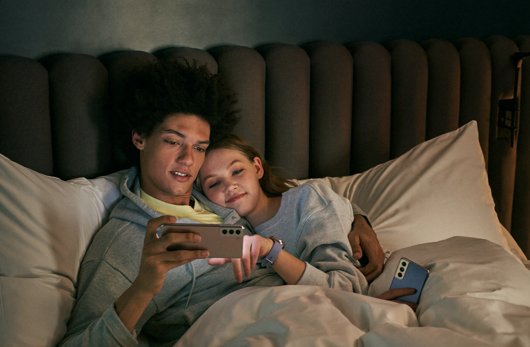A man and a woman lying in bed looking on a phone.