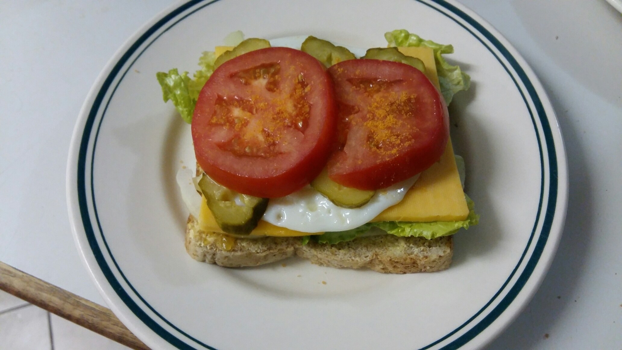 An open-faced sandwich with cheese, tomato, pickles, and lettuce