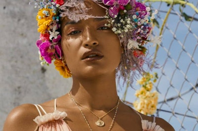 Indya moore posing in a flower crown similar to the one that LGBTQ rights icon Marsha P. Johnson famously wore and wearing a golden chain with Johnson's face on it