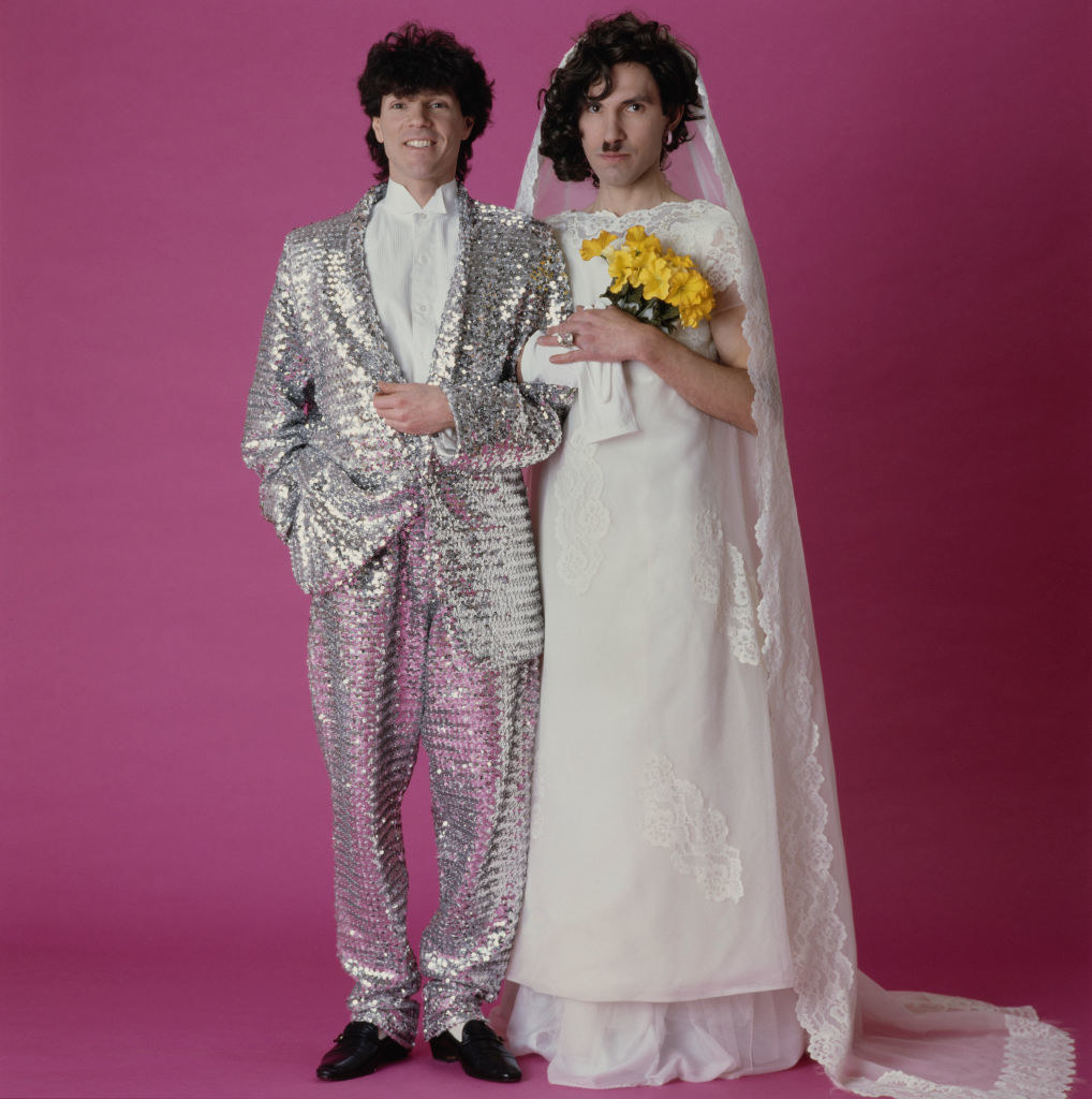 Russel and Ron dressed as a couple getting married in the 1980s, posing for an album cover