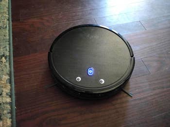 reviewer showing a black robot vacuum on a hardwood floor