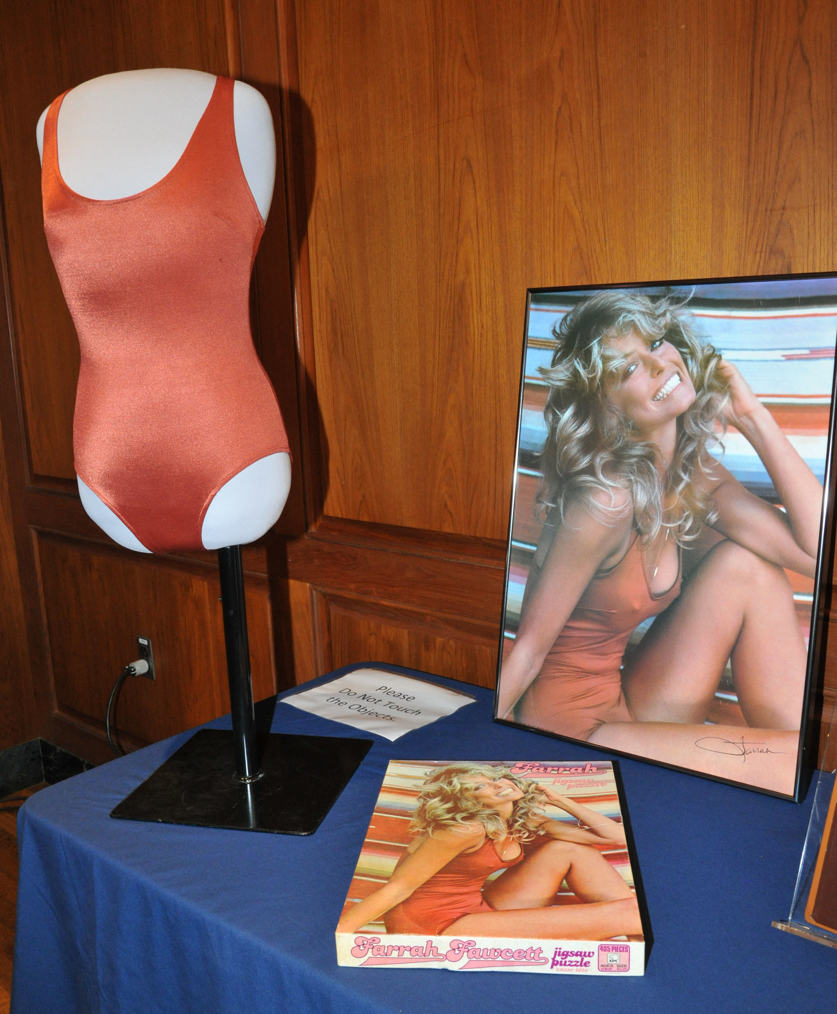 The bathing suit is seen on a mannequin in front of a copy of the poster at the museum 