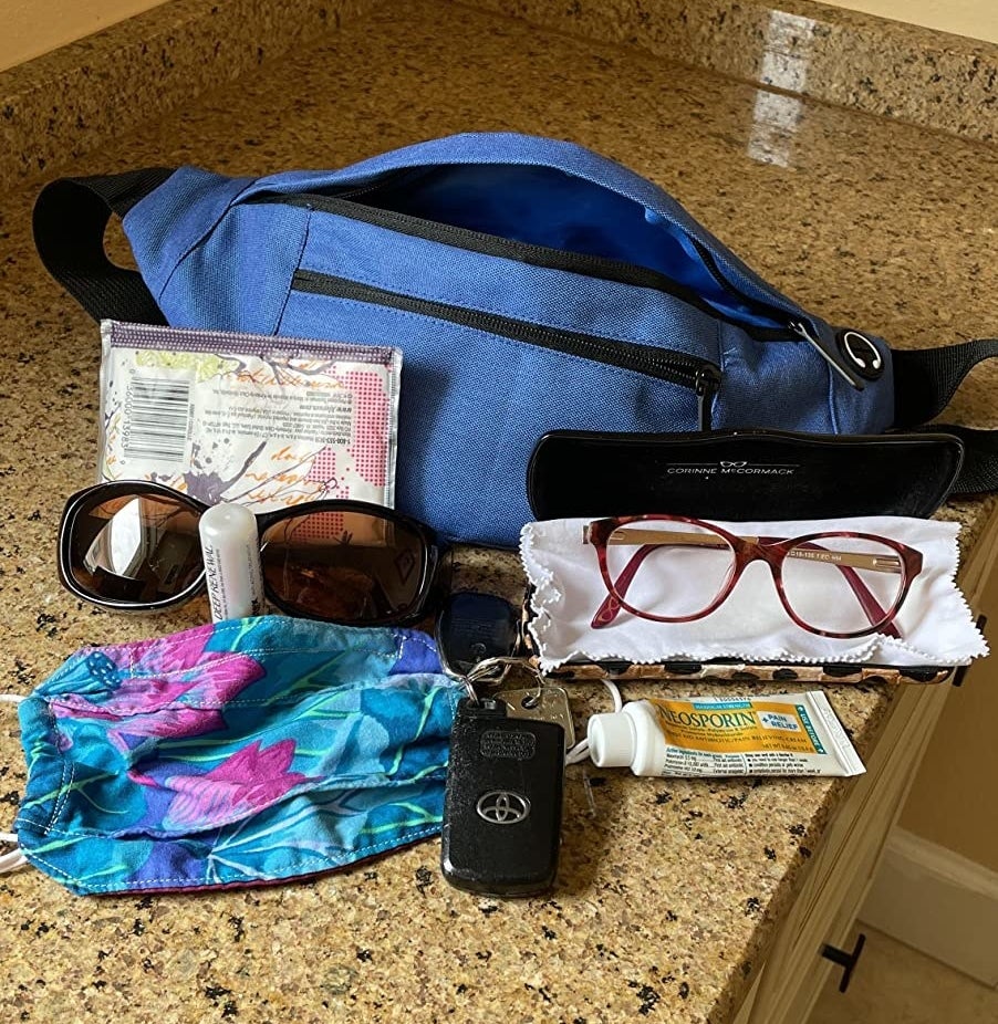 Review&#x27; water blue fanny pack with what it holds: keys, two pairs of glasses, a mask, tissues, lip balm, and neosporin