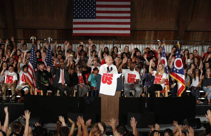 The then vice president surrounded by dozens of college students with their arms raised.