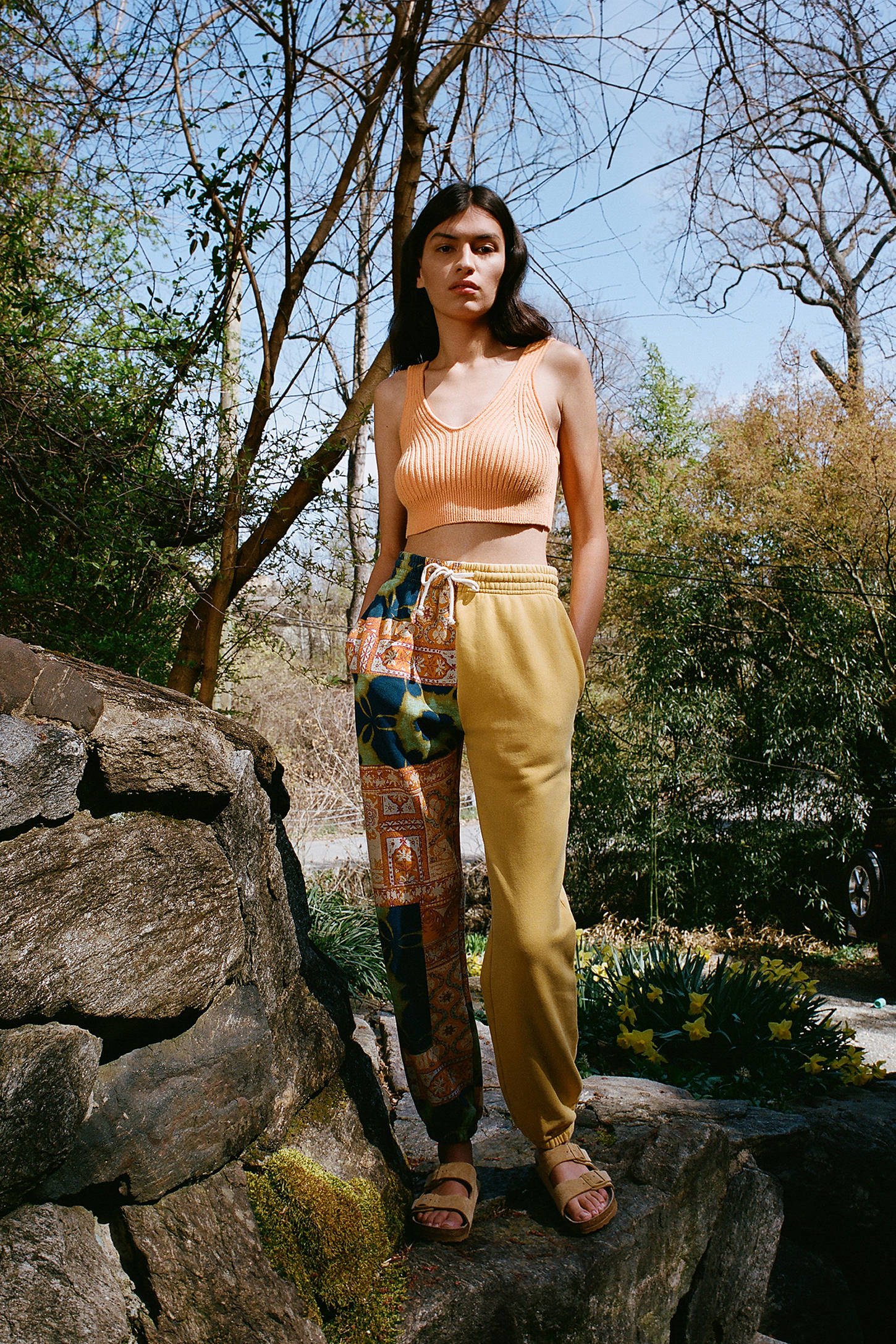 A model wearing the jogger pants with one patchwork print leg and one mustard yellow leg on a hike
