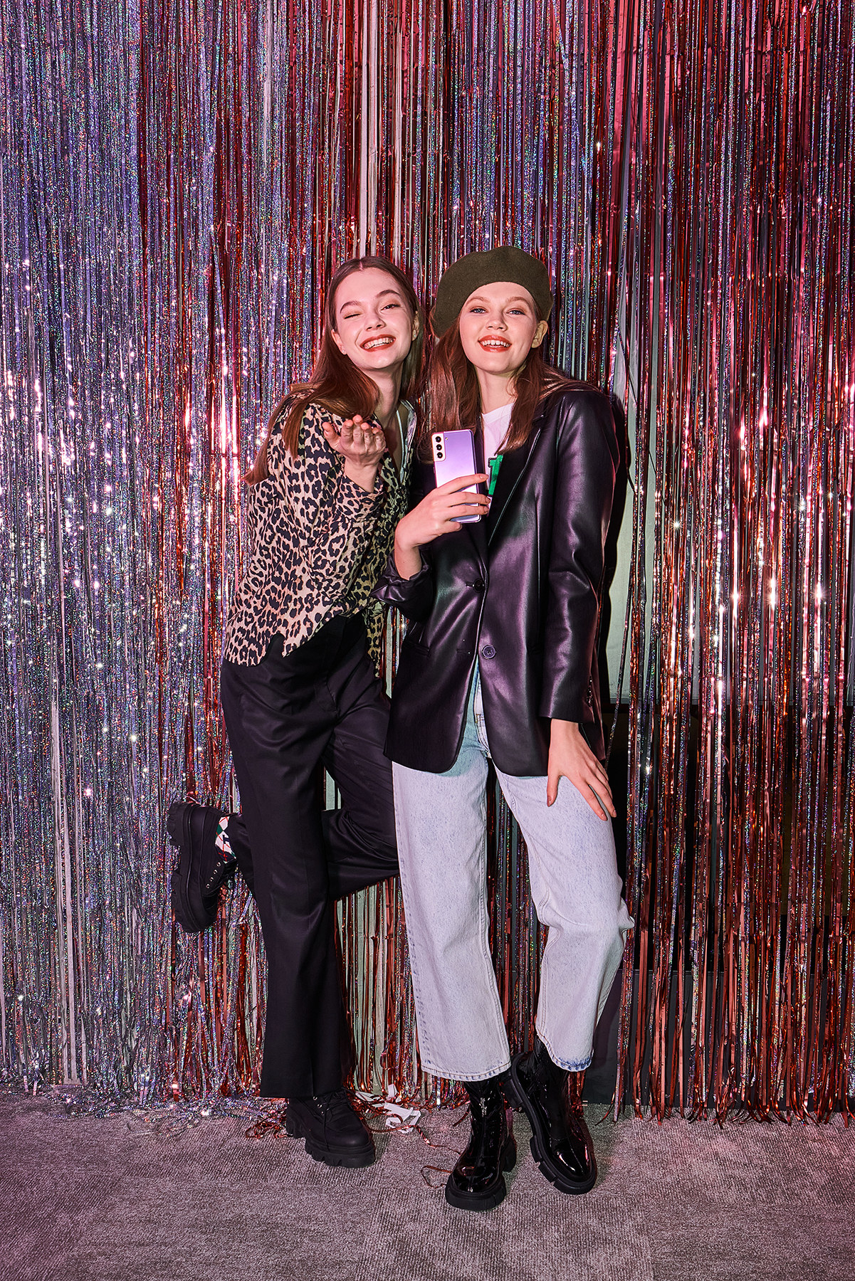 Two women standing in front of a shimmering tinfoil backdrop holding a phone and posing.