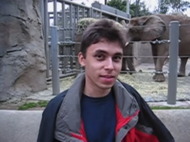 A screenshot from the video of Jawed Karim posing in front of the elephant enclosure