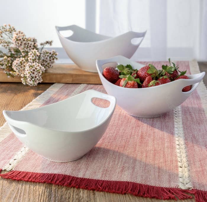 There are three white porcelain curved bowls placed next to each other, and one is holding strawberries