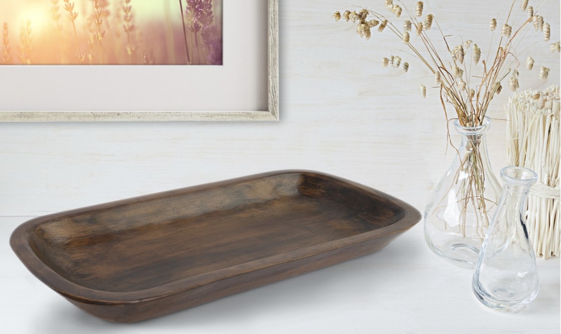 The brown tray with curved edges is on a white table and surrounded by plant-like decor