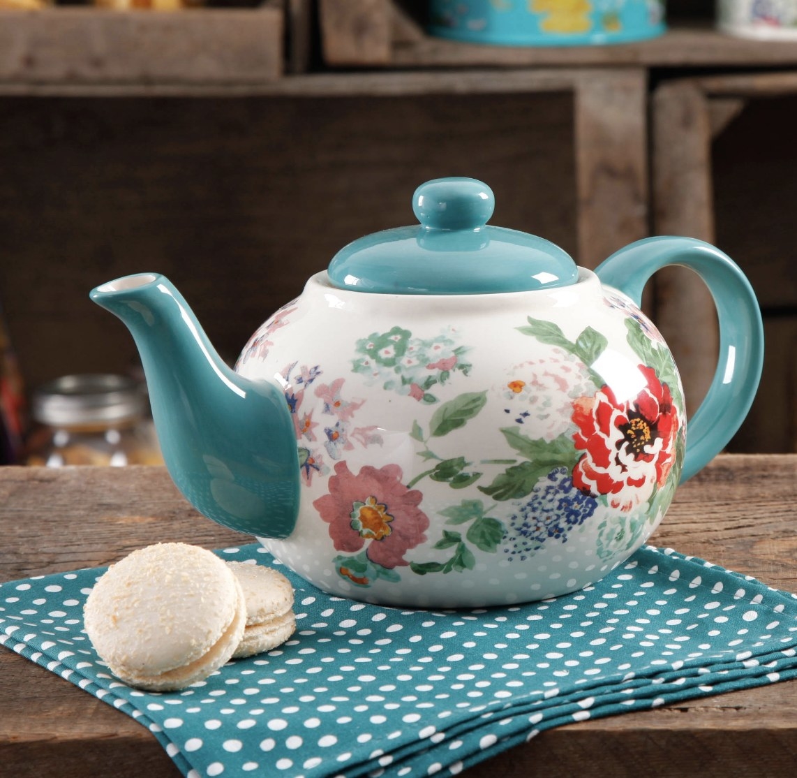 The blue teapot has vibrant floral designs and is atop a blue and white polka dot hand towel