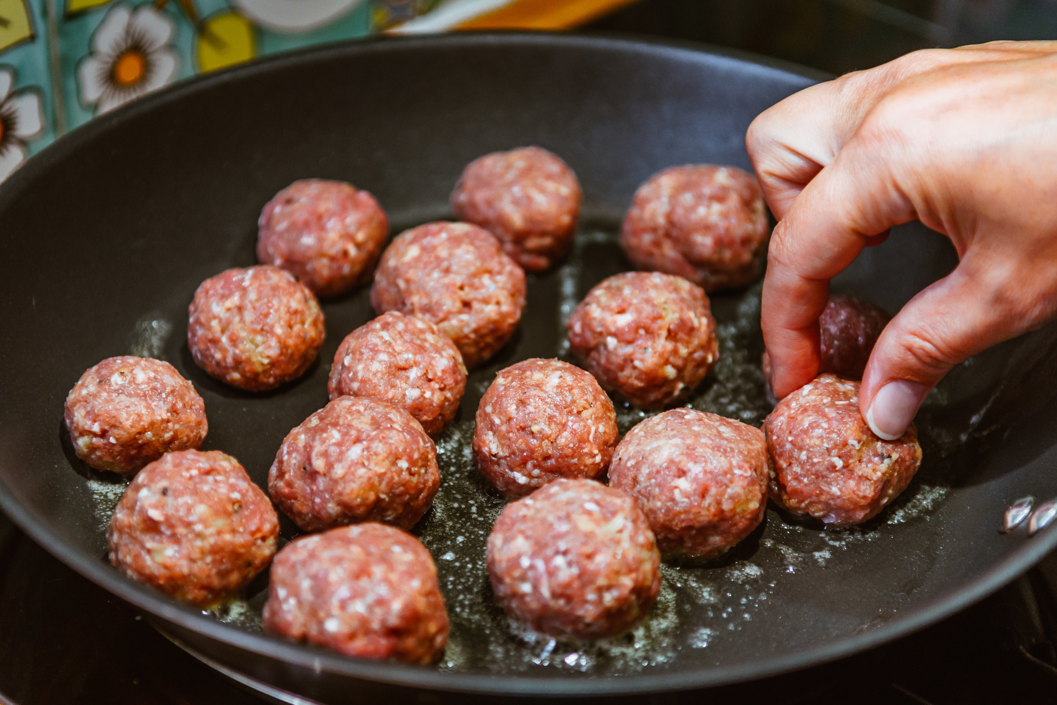 Placing raw meatballs into a frying pan.