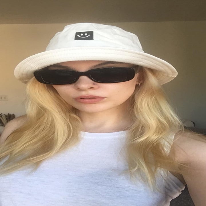reviewer wears same style sunglasses while wearing a white bucket hat