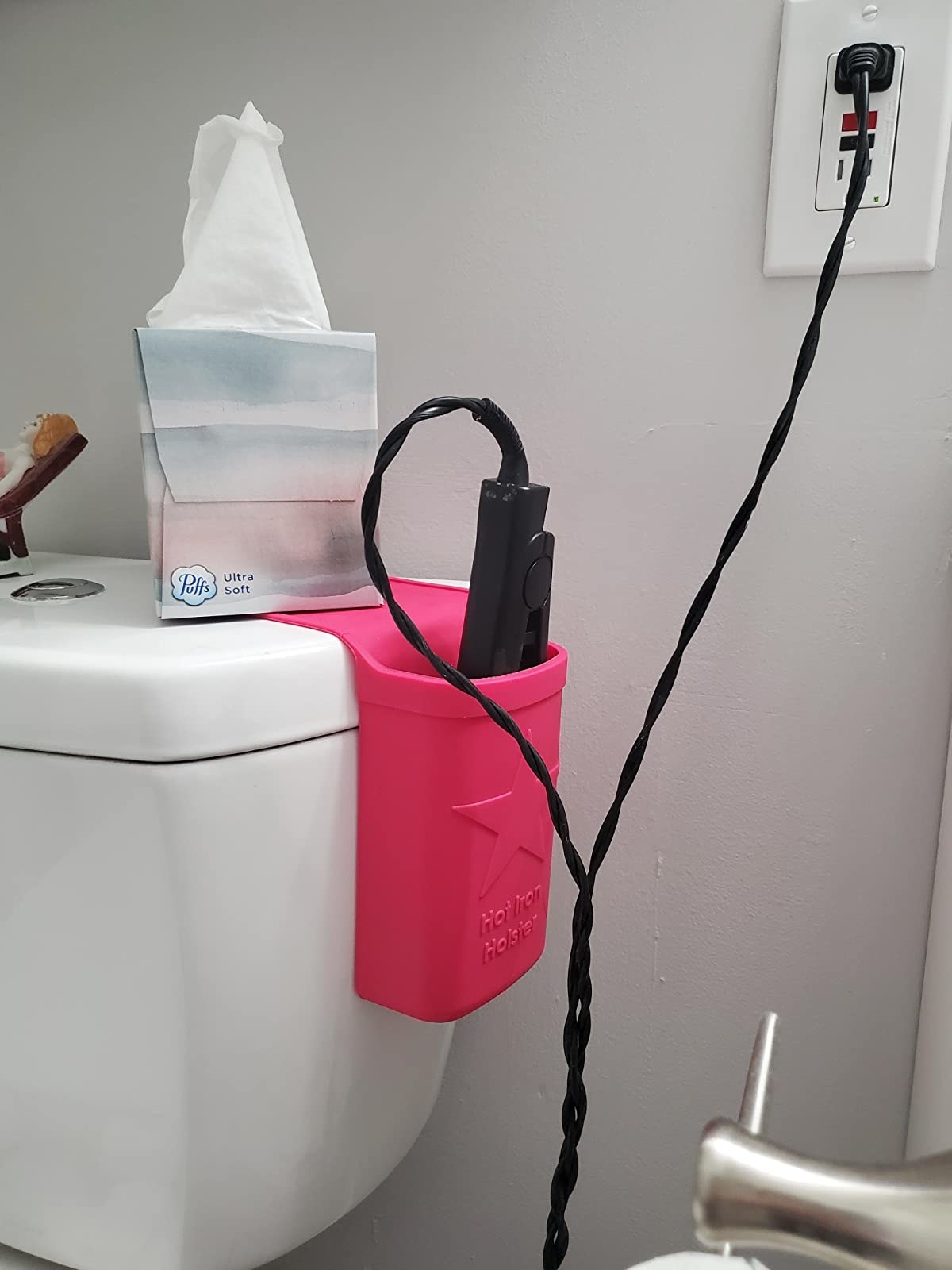 reviewer showing a pink hot iron holder holding a flat iron that's plugged in