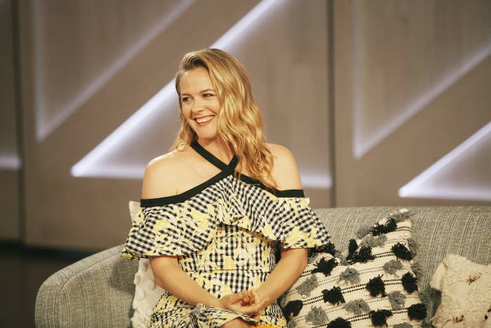 Alicia Silverstone smiles and sits on a couch on set of "The Kelly Clarkson Show"