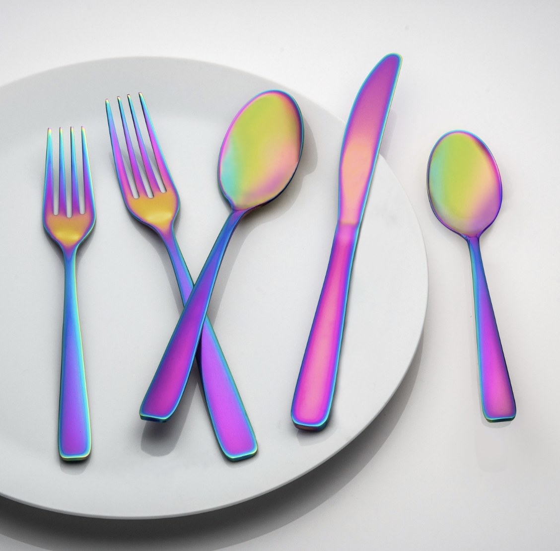 Five pieces of bright blue, purple and gold-toned silverware are laid across a plate and white surface