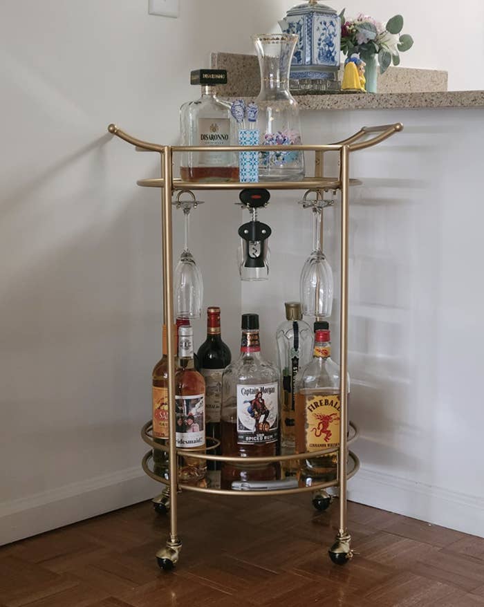 Reviewer&#x27;s bar cart sits in the corner of a dining room and is holding various liquor bottles and barware