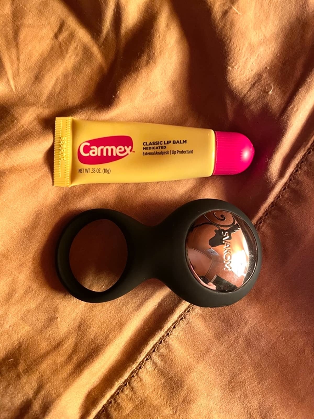 Black vibrating cock ring next to tube of lip balm for size comparison