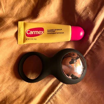 Black vibrating cock ring next to tube of lip balm for size comparison