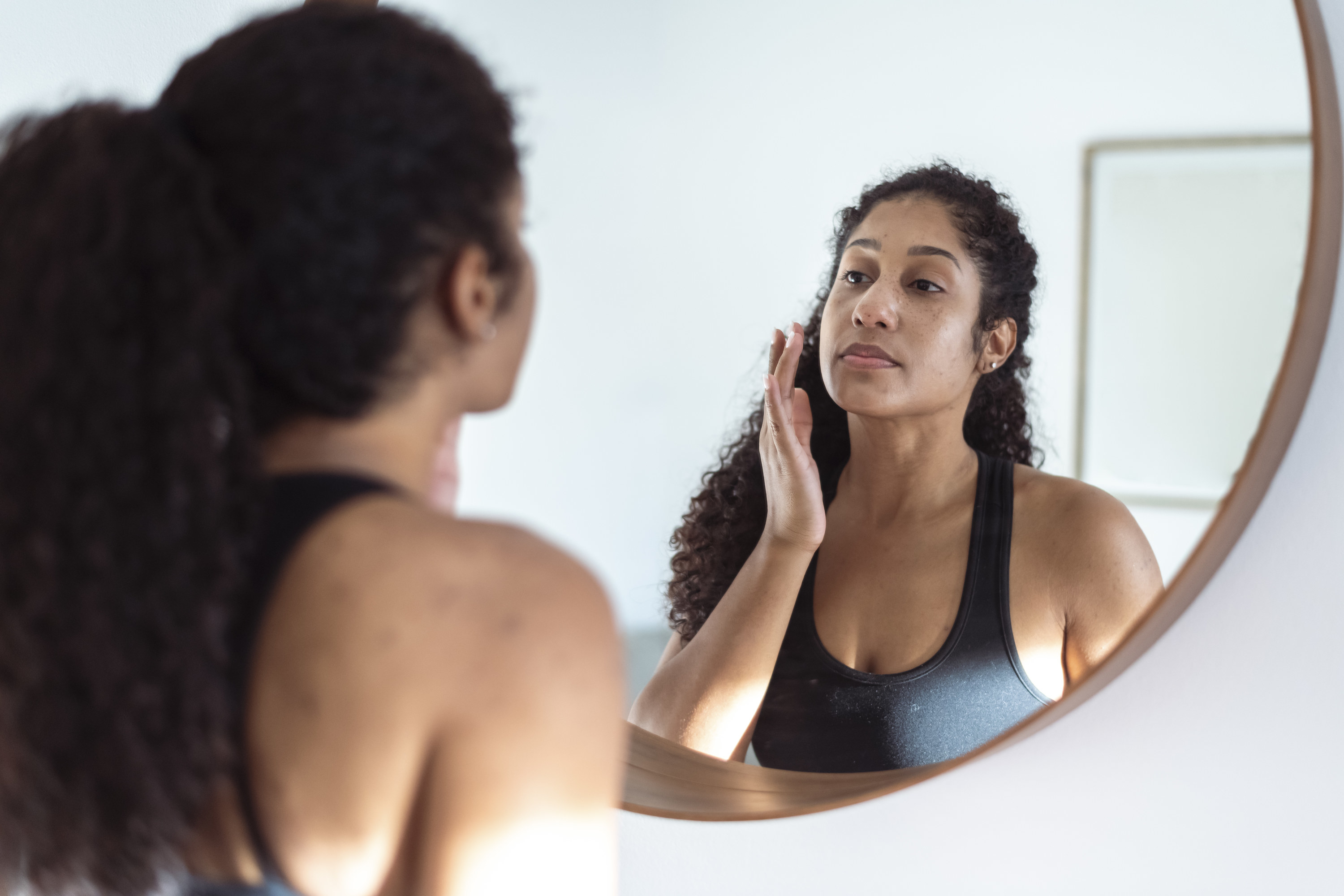 A person touching their cheek in the mirror