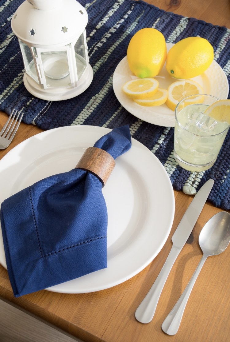 The wooden napkin ring is around a blue napkin and  surrounded by lemons and silverware