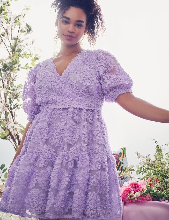 model wearing purple dress with bow tie in back and poofy sleeves