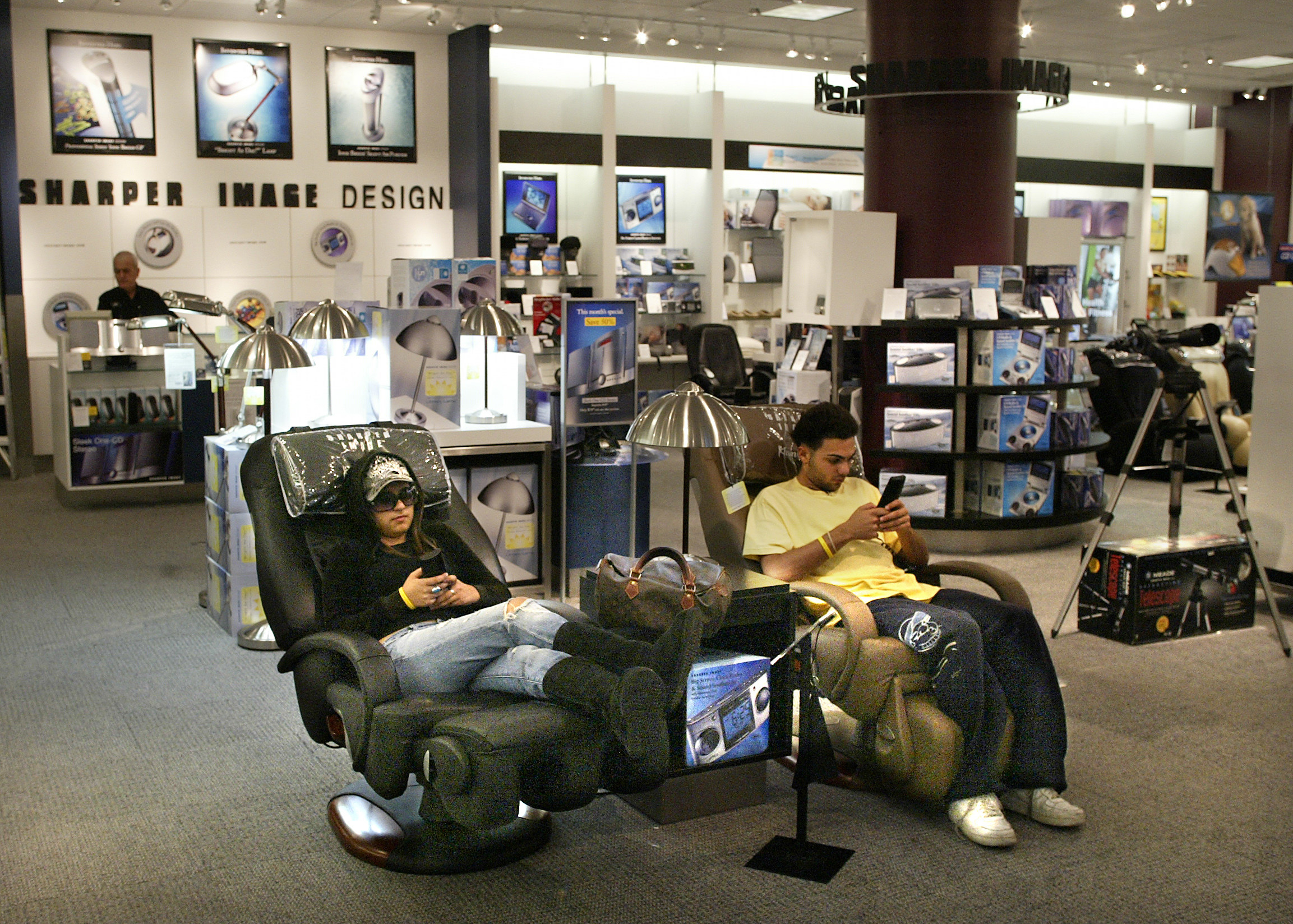Two teens sitting in massage chairs inside a Sharper Image