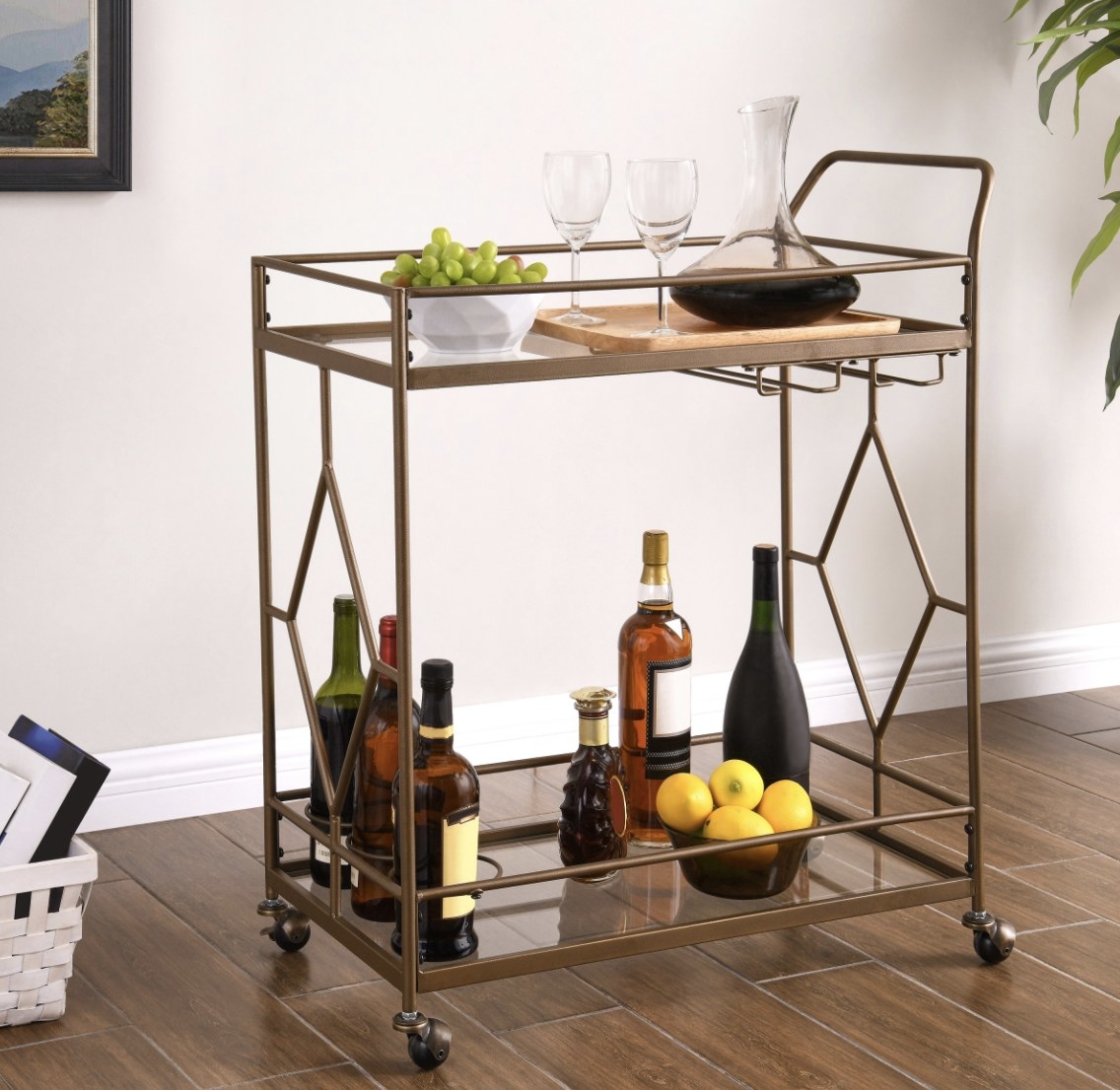 The brass bar cart with geometric shapes is holding bottles, fruit and glasses