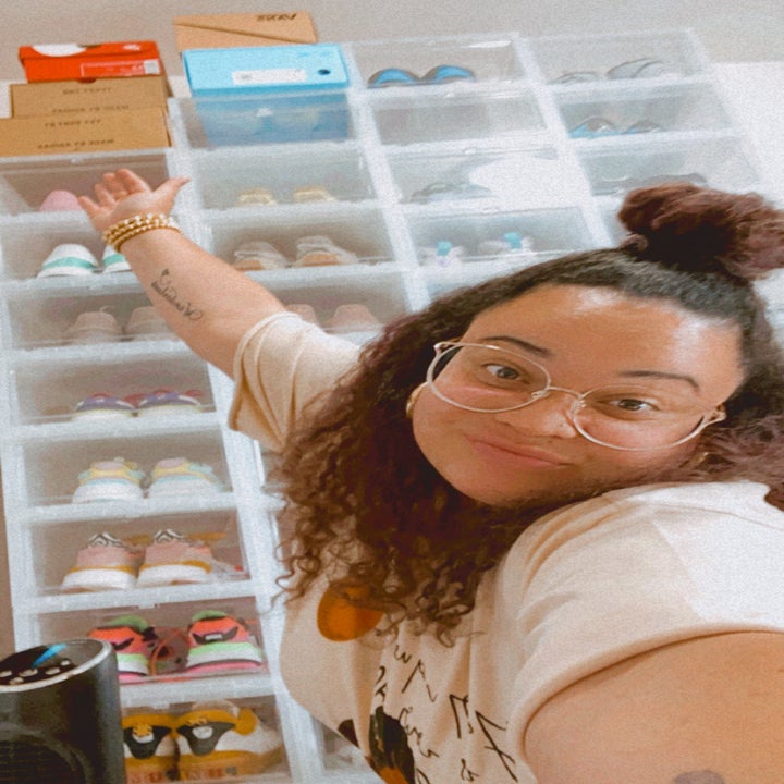 buzzfeed editor smiling and gesturing to her shoe wall 