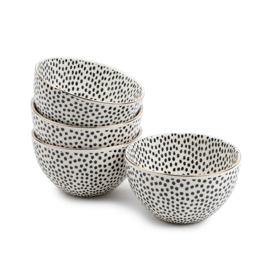 There are four black and white dotted bowls with gold rimmed edges