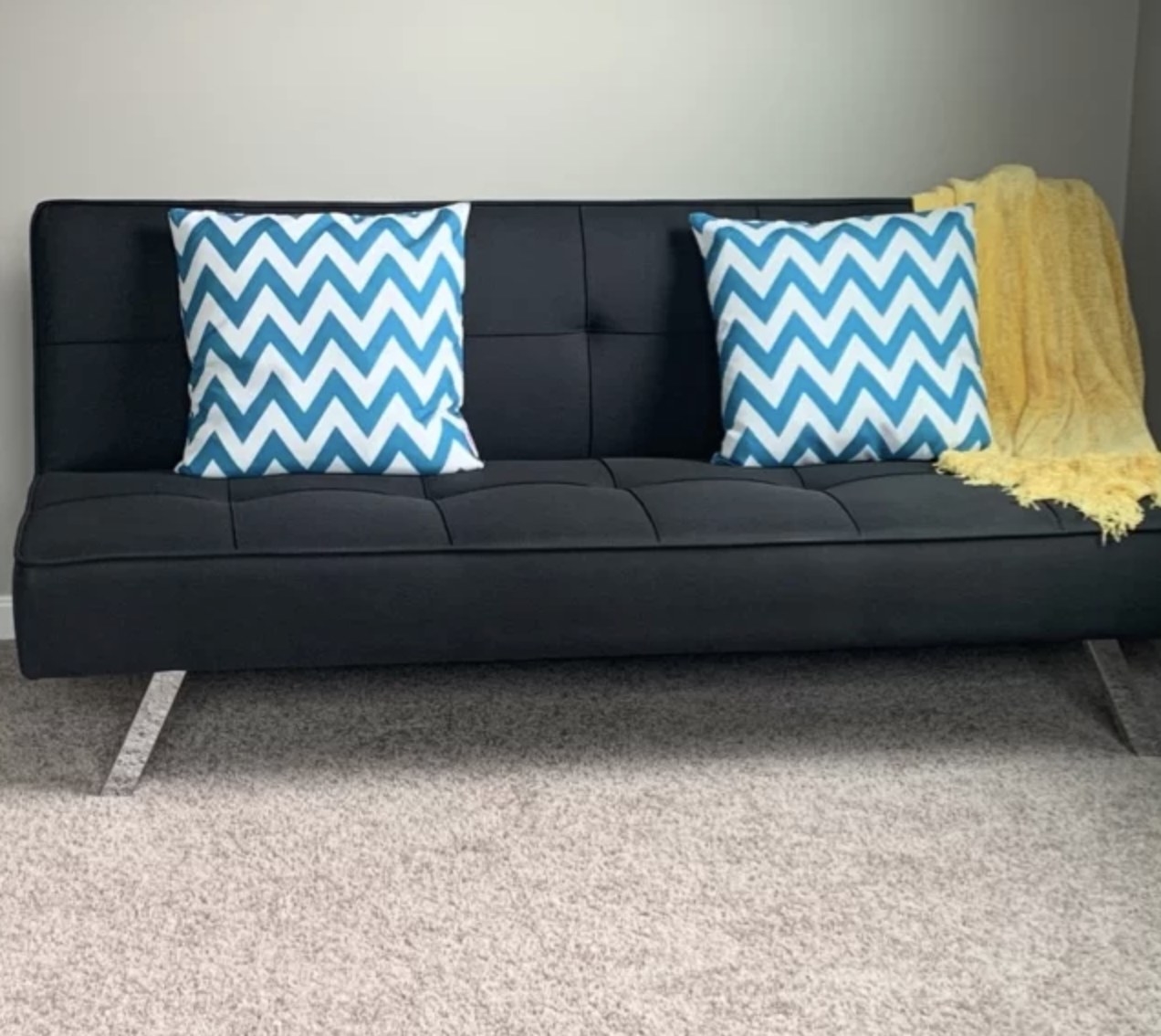 A reviewer&#x27;s black Serta futon with blue pillows on it