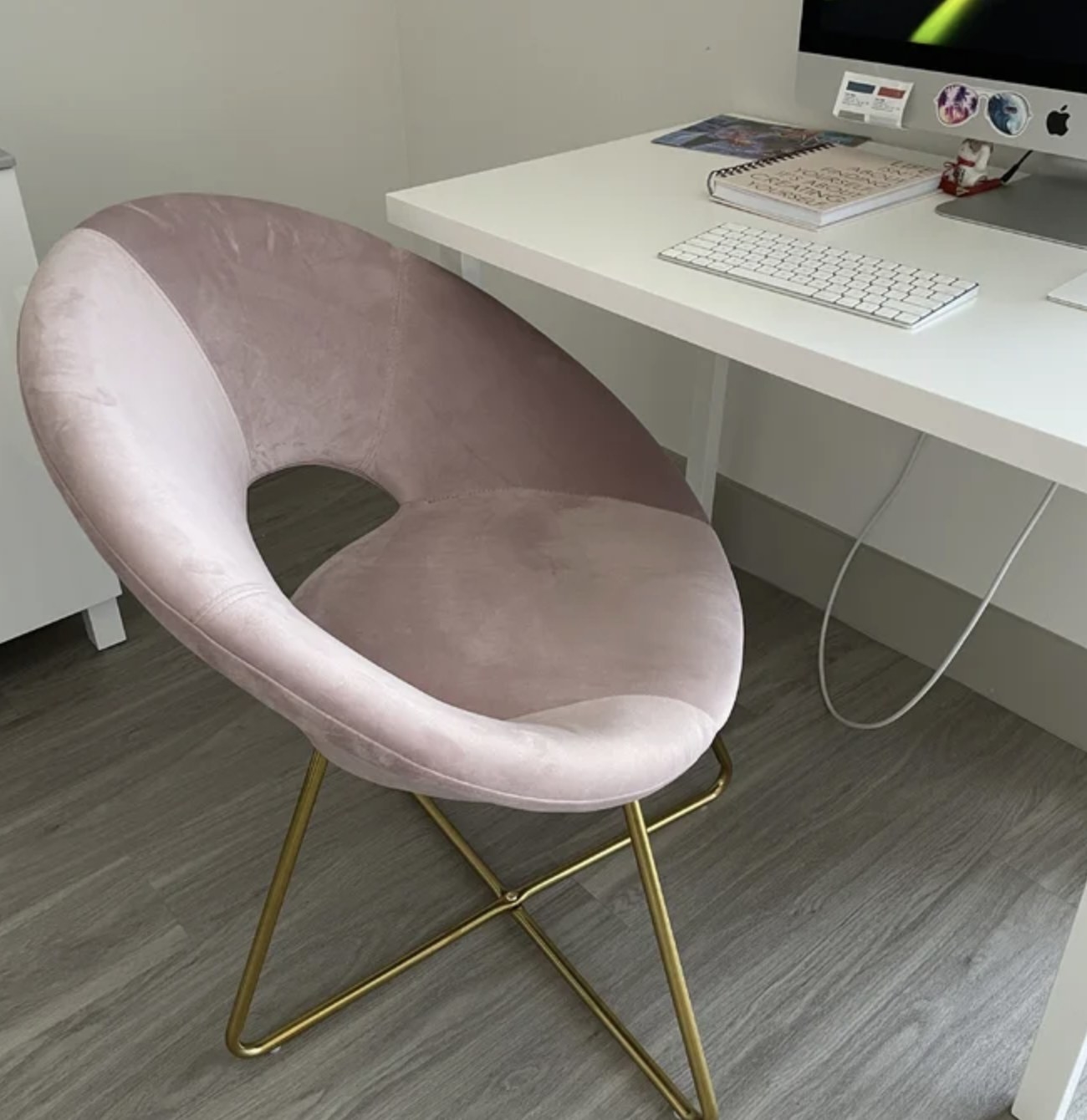 A reviewer&#x27;s round pink velvet accent chair with gold metal legs in front of a computer desk