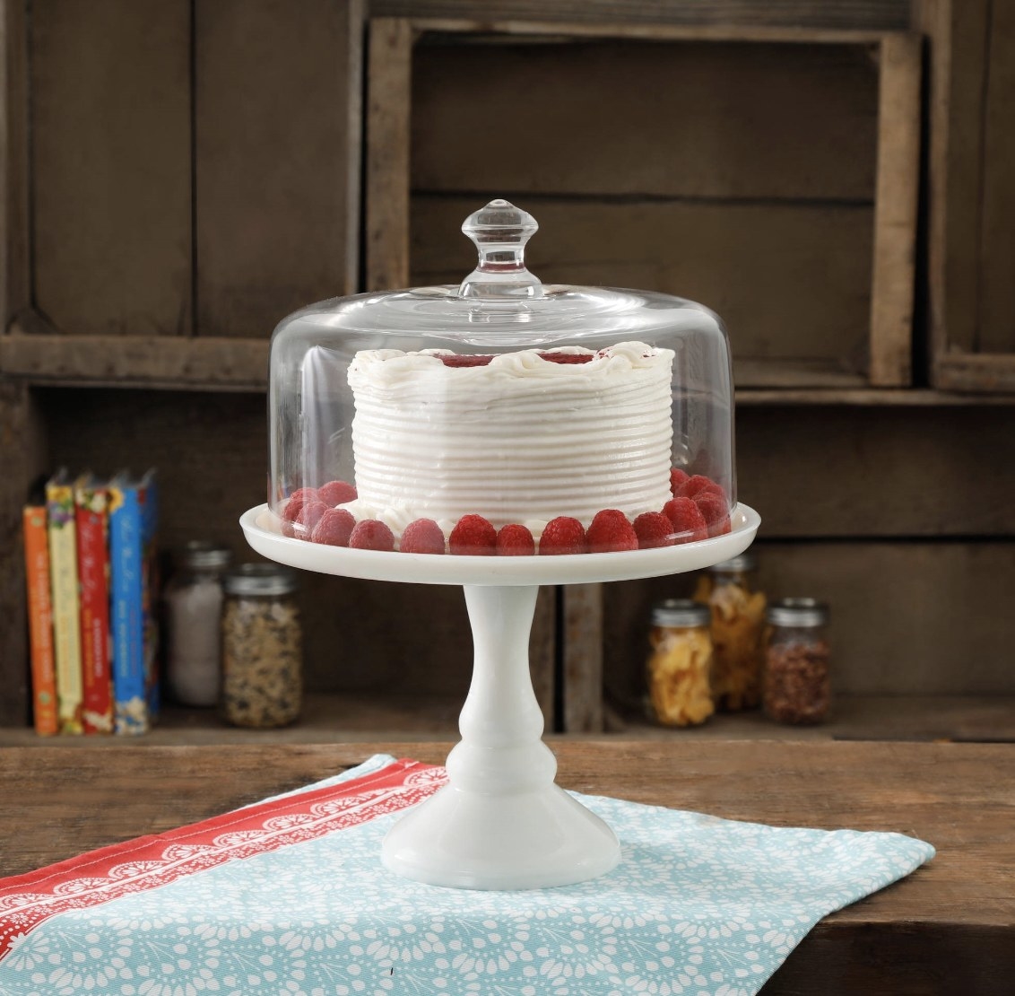 The white cake stand has a milky white base and is holding a white frosted cake with raspberries
