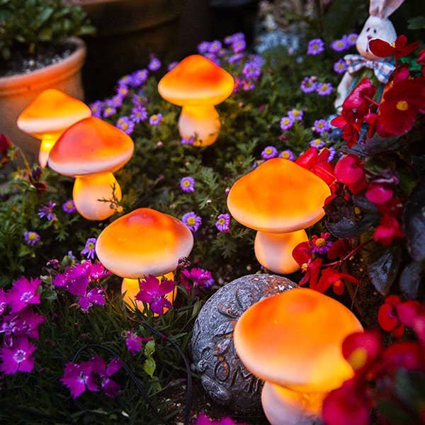 six of the mushroom-shaped solar lights glowing in a flower bed outdoors
