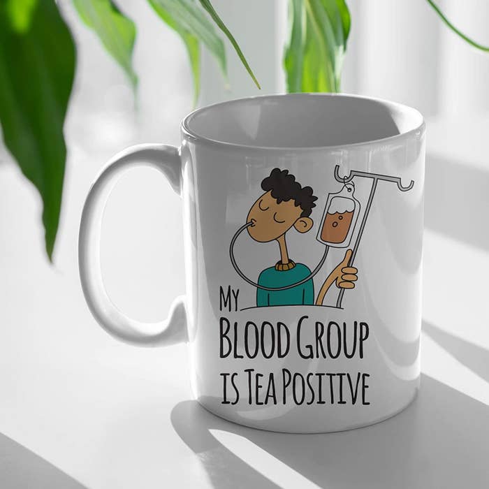 A coffee mug with an illustration of a man drinking tea from an IV drip and text that says &#x27;My blood group is Tea Positive.&#x27;