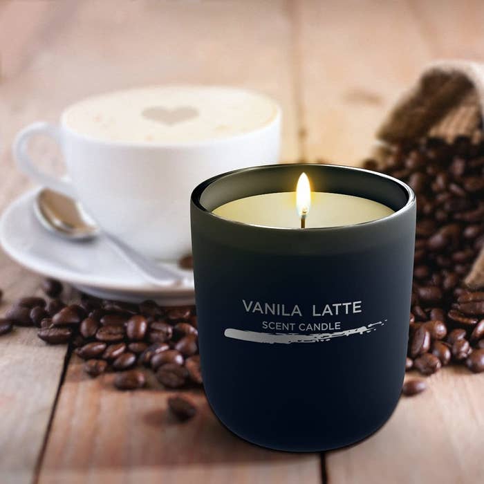 A Miniso candle in a black jar with a vanilla latte coffee in the background.