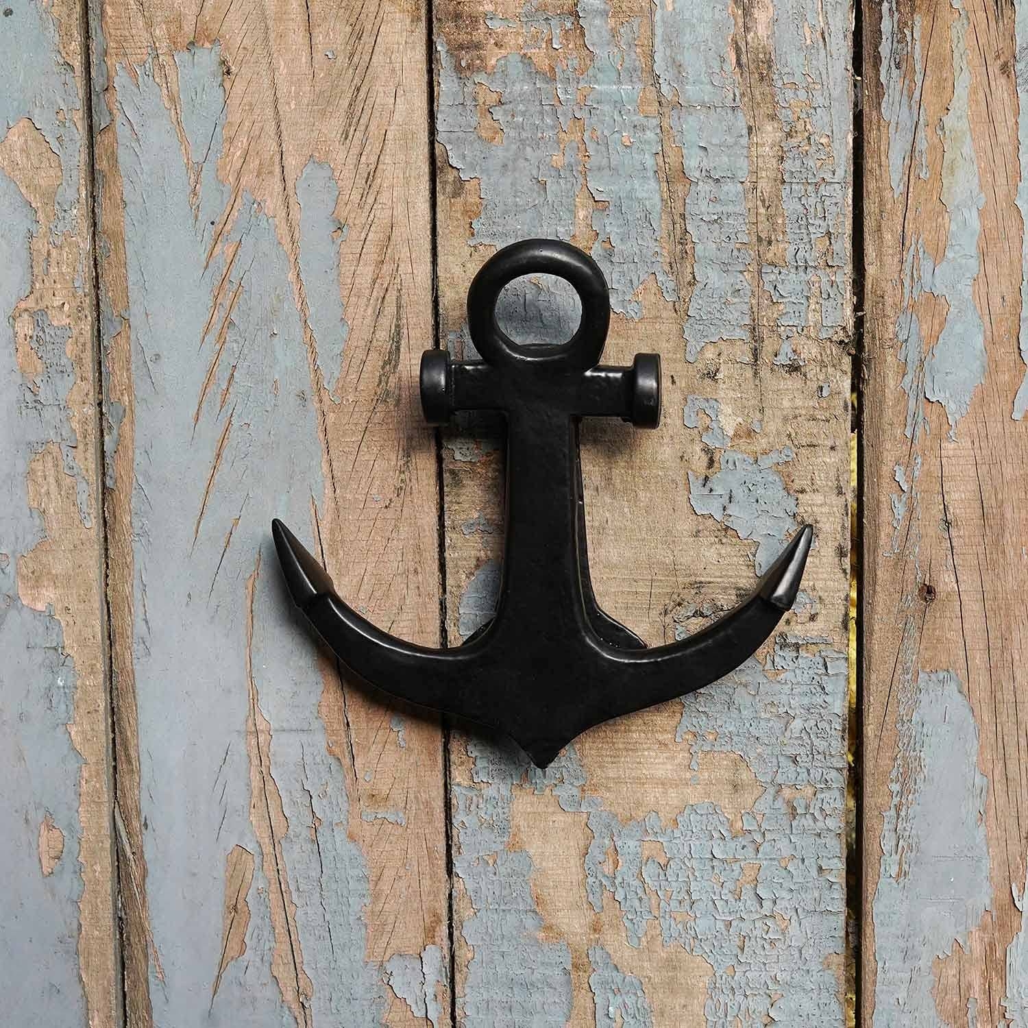 A solid black anchor-shaped door knocker attached to a wooden surface. 
