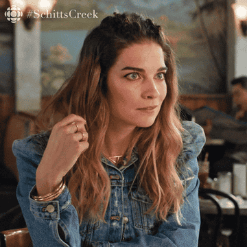 GIF of Annie Murphy from Schitt&#x27;s Creek putting her chin in her hands in anticipation of hearing something interesting