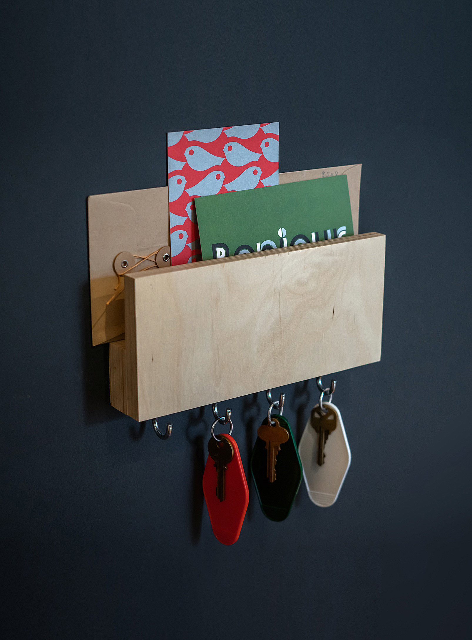 A small wooden shelf with letters stored at the top and keys hanging from four hooks on the bottom