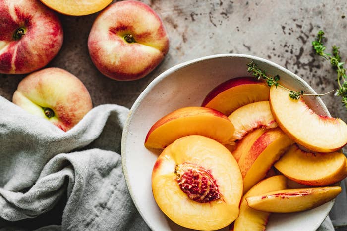 Peaches on a counter next to sliced peaches in a bowl