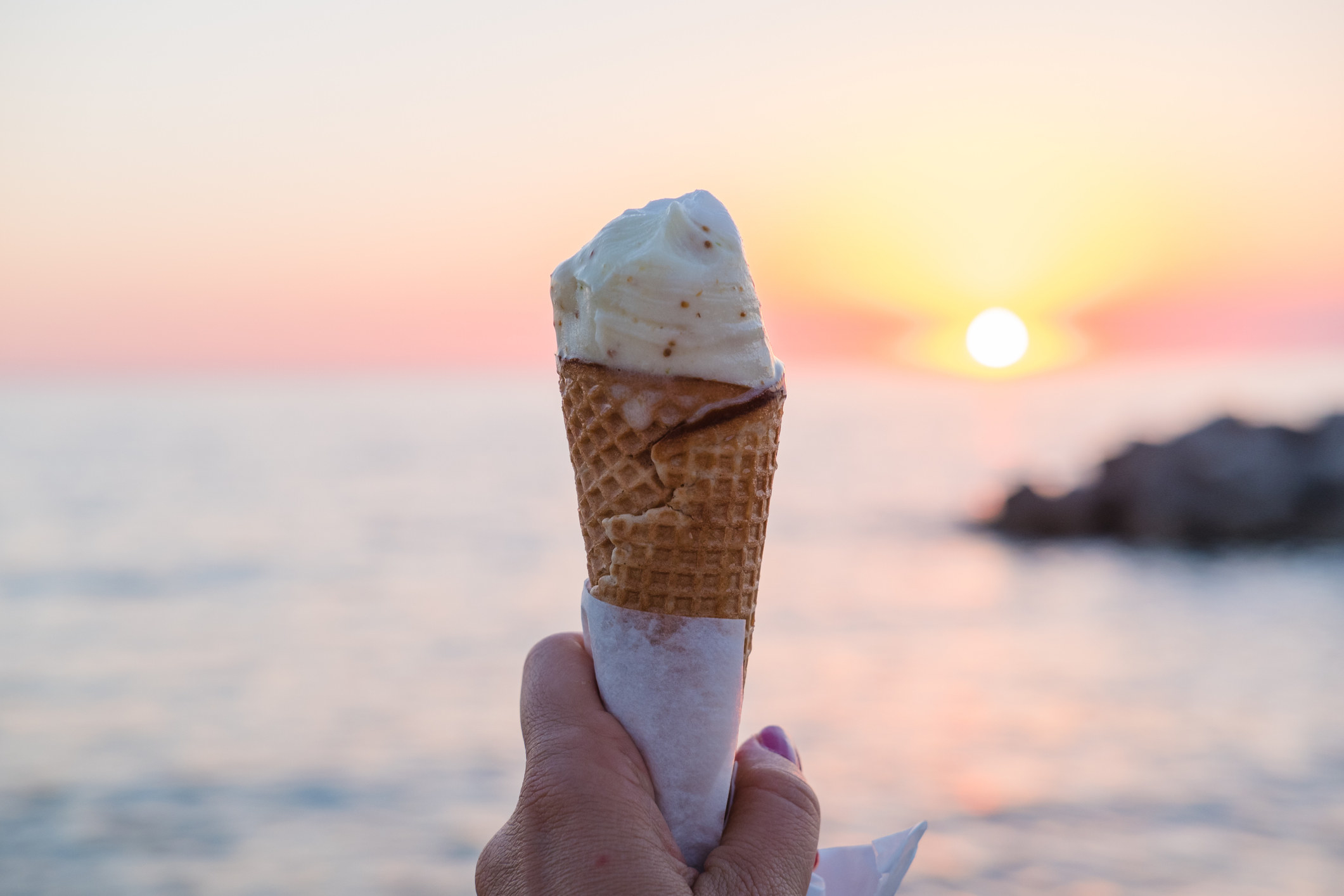 a person holding an ice cream cone in front of a scenic sunset by a lake 
